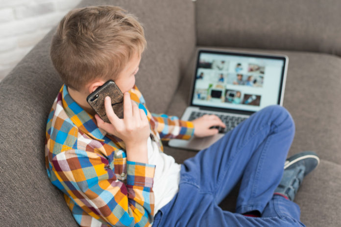boy-using-laptop-couch-making-phone-call